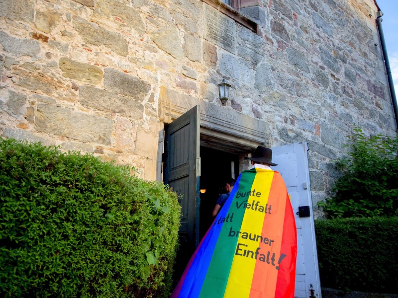 Eine Teilnehmerin der Gegendemonstration zum Festival steht mit einem Regenbogenumhang in der Stadtkirche St. Bartholomäus in Themar am Kircheneingang.