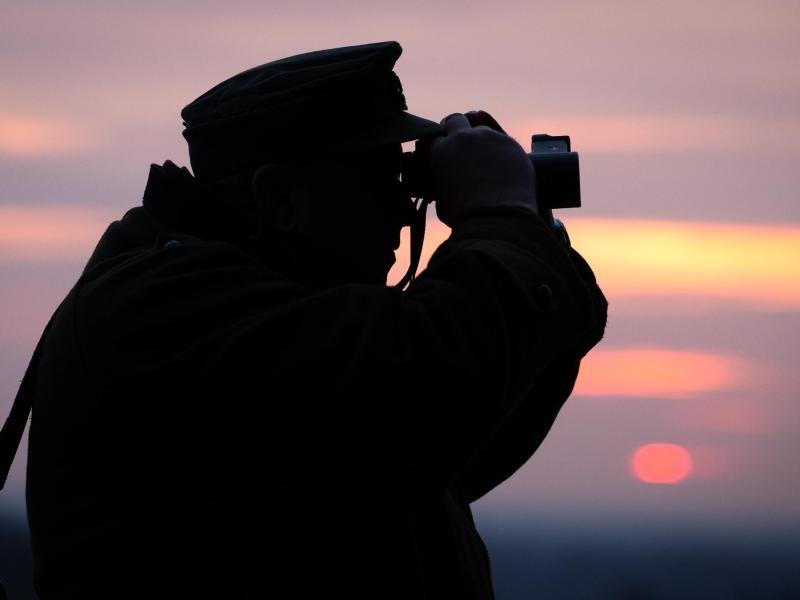 Ein Jäger blickt durch sein Fernglas in der Abenddämmerung.