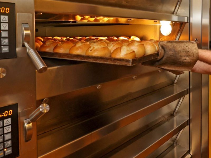Bäcker nimmt frische Brötchen aus dem Ofen