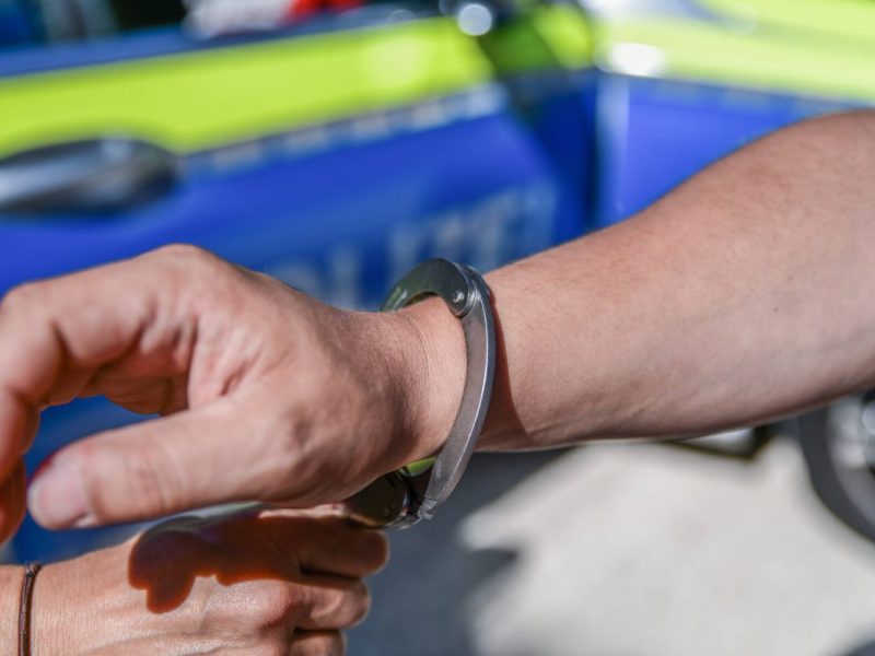 Mann bekommt vor Streifenwagen Handschellen angelegt