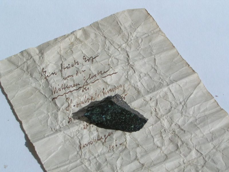Ein Stück Papier gibt den Hinweis auf die Herkunft eines kleinen Metallstücks.